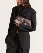 Kassandre Colonne clutch in brown python-effect leather with gold hardware, worn view